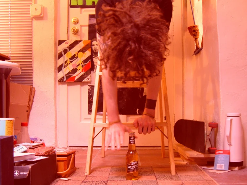 Josh descends a ladder upside-down to pick up a beer placed on the floor.