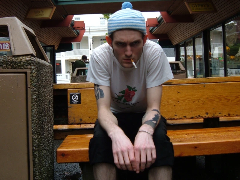 Josh smokes on a bench with a no-smoking sign.