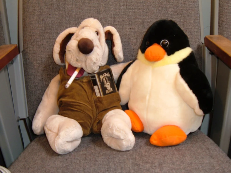 A stuffed dog and penguin share a movie theatre seat.